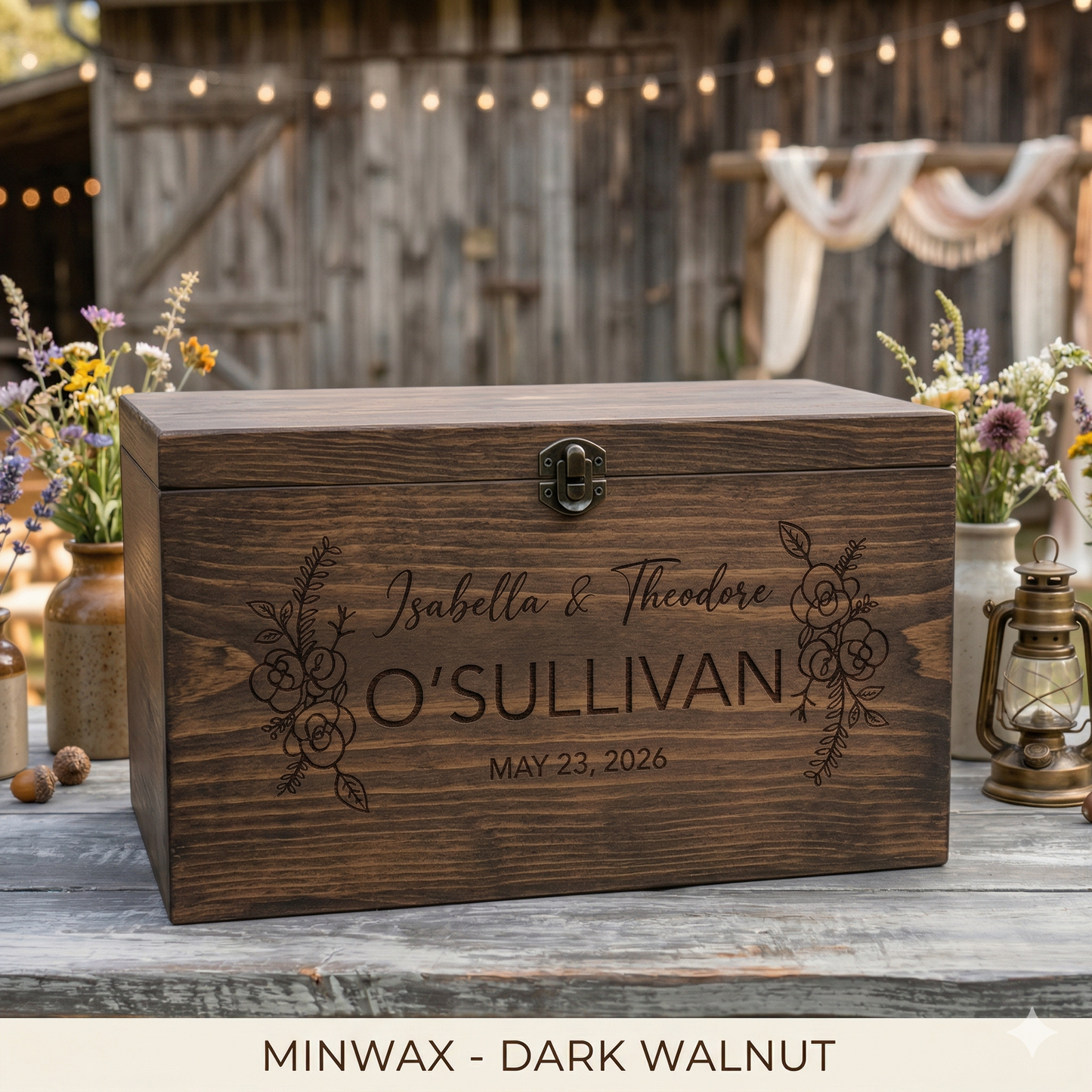 Wooden box with engraved names and date, set outdoors with flowers and lanterns.